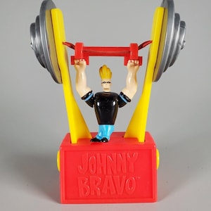Peut inclure: Une figurine en plastique Johnny Bravo montée sur une base rectangulaire rouge avec le texte JOHNNY BRAVO en relief sur le devant. La figurine soulève une grande barre avec des poids argentés, des bras de support jaunes et une barre transversale rouge.