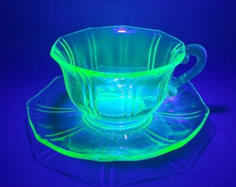 Juego de taza y platillo de vidrio de vaselina de uranio vintage que brilla bajo la luz ultravioleta. Época de la Gran Depresión.