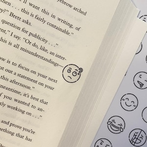 Könnte beinhalten: Eine Buchseite mit einem schwarz-weißen Emoji-Aufkleber eines verwirrten Gesichts mit einem Fragezeichen. Zusätzliche Emoji-Aufkleber sind auf weißem Hintergrund sichtbar.