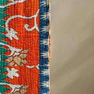 May include: A colorful kantha quilt with a floral pattern in shades of orange, white, blue, and green. The quilt is hand-stitched and has a unique, rustic look.
