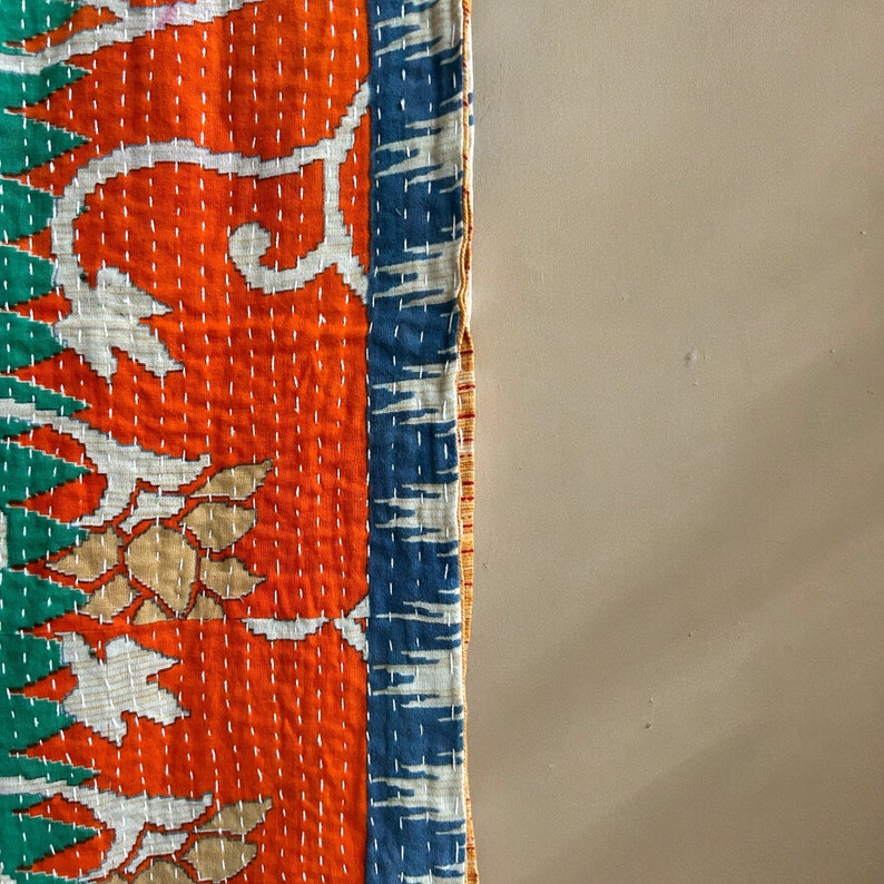 May include: A colorful kantha quilt with a floral pattern in shades of orange, white, blue, and green. The quilt is hand-stitched and has a unique, rustic look.