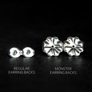 May include: Two pairs of earring backs, one pair is regular and the other is monster. The regular earring backs are small and round, while the monster earring backs are larger and have a flower-like design.