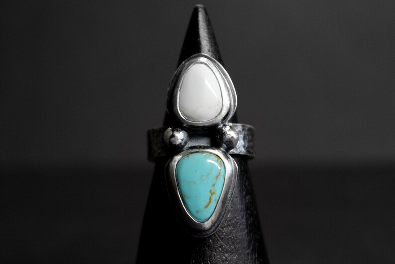 May include: A silver ring with two teardrop-shaped stones. The top stone is white and the bottom stone is turquoise.
