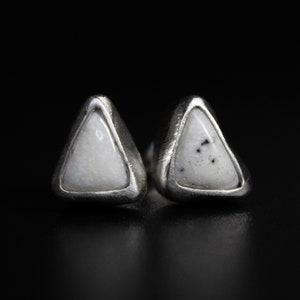 Può includere: Un paio di orecchini a lobo in argento a forma di triangolo con accenti di pietra bianca. Le pietre hanno un motivo maculato.