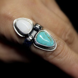 May include: A silver ring with two teardrop-shaped stones. The larger stone is turquoise blue, and the smaller stone is white.