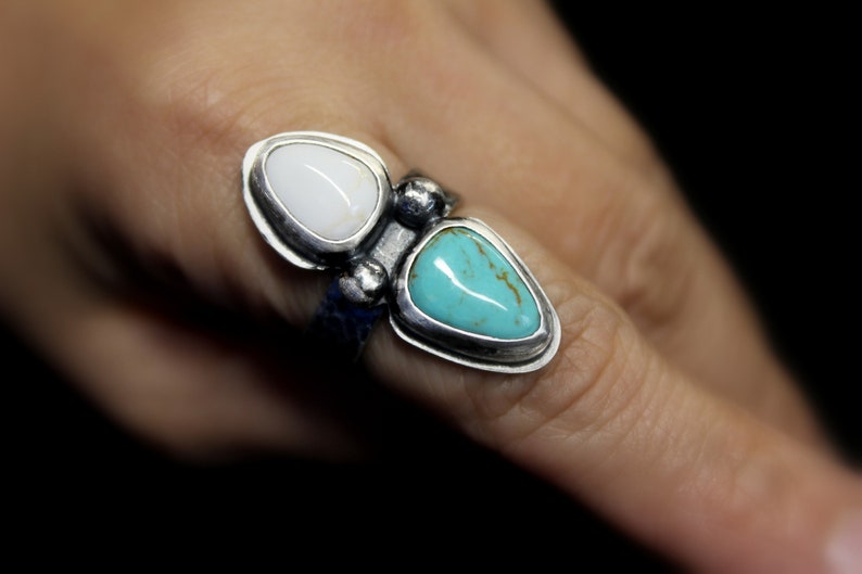 May include: A silver ring with two teardrop-shaped stones. The larger stone is turquoise blue, and the smaller stone is white.