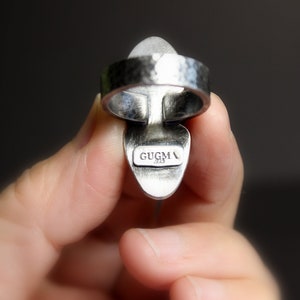May include: Silver ring with a hammered band and a clear stone set in a silver setting. The ring is marked "GUGMA 925" on the back.