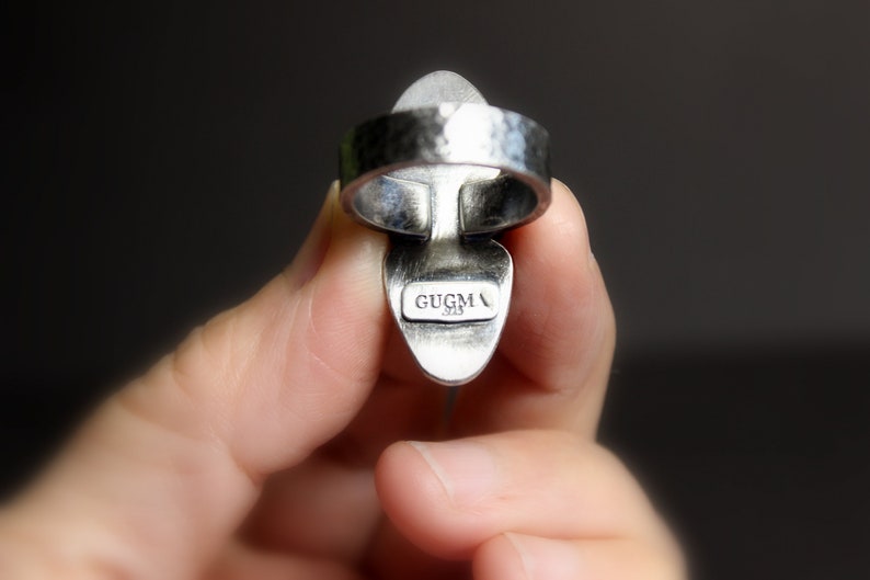 May include: Silver ring with a hammered band and a clear stone set in a silver setting. The ring is marked "GUGMA 925" on the back.