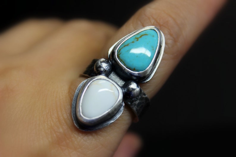 May include: A silver ring with two teardrop-shaped stones. The top stone is turquoise blue, and the bottom stone is white.