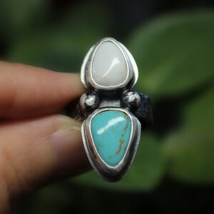 May include: A silver ring with a turquoise and white stone set in a pointed shape.