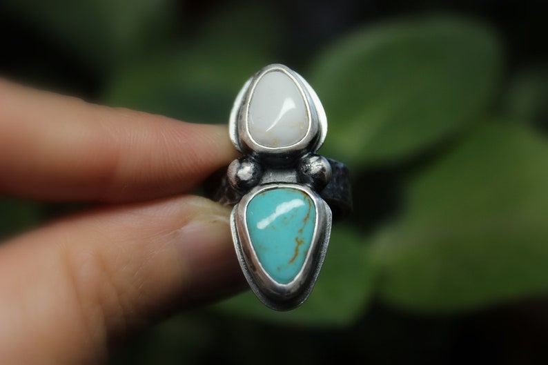May include: A silver ring with a turquoise and white stone set in a pointed shape.
