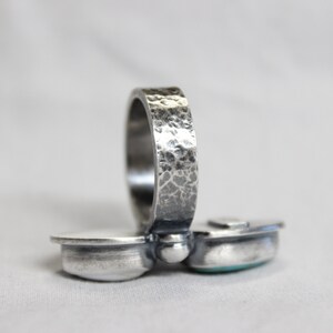 May include: A silver ring with a hammered band and two turquoise stones set in the front. The ring is designed to be worn on the knuckle.