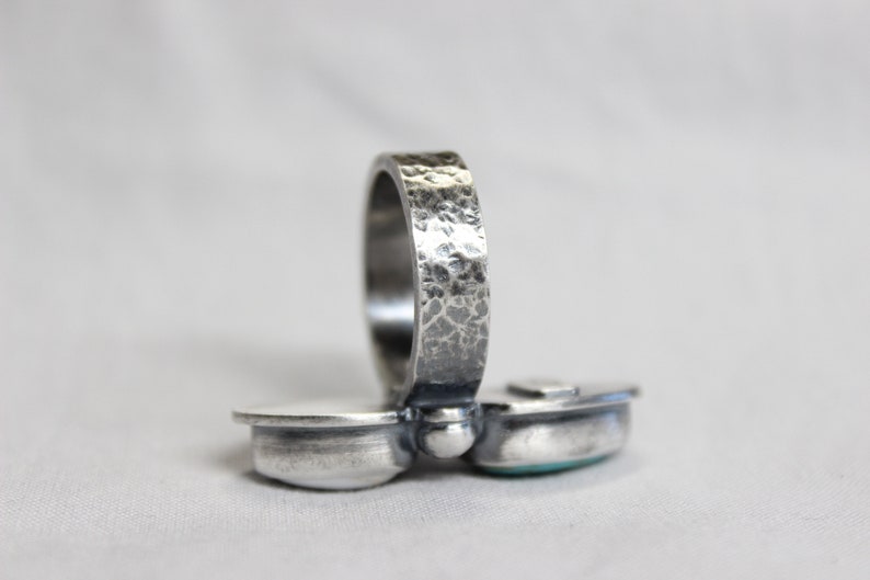 May include: A silver ring with a hammered band and two turquoise stones set in the front. The ring is designed to be worn on the knuckle.