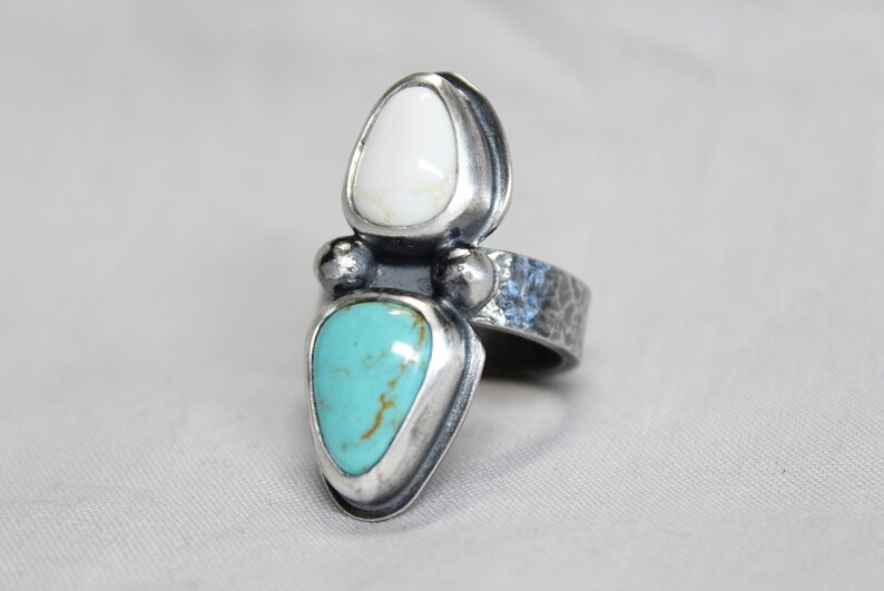 May include: A silver ring with a turquoise and white stone setting. The ring band is textured and has a hammered finish.