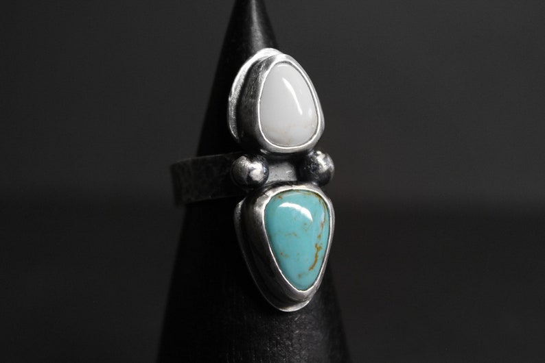 May include: A silver ring with a white and turquoise stone setting. The stones are set in a teardrop shape and are surrounded by silver.