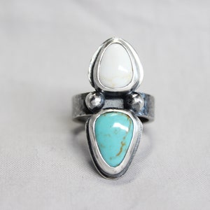 May include: A silver ring with two teardrop-shaped stones. The top stone is white and the bottom stone is turquoise.