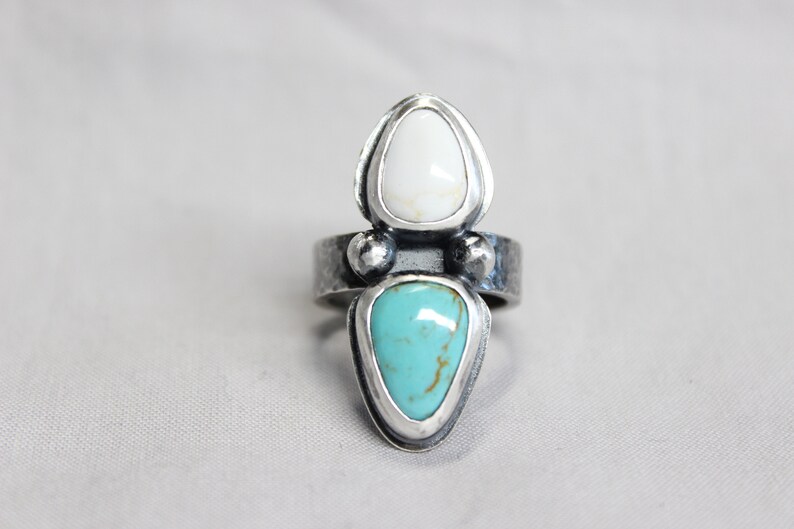 May include: A silver ring with two teardrop-shaped stones. The top stone is white and the bottom stone is turquoise.