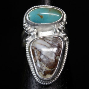 Puede incluir: Un anillo de plata con dos piedras. La piedra superior es un óvalo turquesa, y la piedra inferior es una ágata marrón y blanca.
