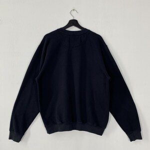 May include: A black crew neck sweatshirt hanging on a black hanger against a white wall. The sweatshirt has long sleeves and a ribbed hem and cuffs. The back of the sweatshirt is visible, showing a plain design.