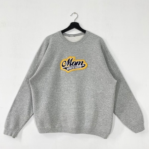 Puede incluir: Una sudadera gris con mangas largas, colgada de una percha negra. La sudadera presenta la palabra "Mom" en un parche amarillo y azul, con "University of Washington" debajo.