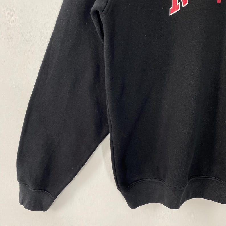May include: Black sweatshirt with red and white lettering. The sweatshirt has long sleeves and a crew neck. The lettering appears to be a stylized initial or logo. The fabric appears to be a soft, medium-weight material.
