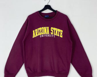 May include: A maroon sweatshirt with the words "ARIZONA STATE UNIVERSITY" in yellow block letters. The sweatshirt is hanging on a black hanger against a white background. The sweatshirt has long sleeves and a crew neck.