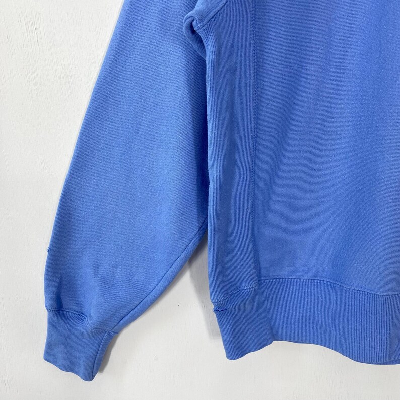 Peut inclure: Un sweat-shirt bleu clair avec des poignets et un ourlet c&ocirc;tel&eacute;s. La manche longue est visible, montrant le tissu doux et le d&eacute;tail de la couture. Le v&ecirc;tement est de couleur unie, avec un design simple et classique.