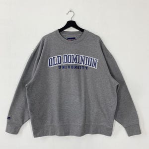 May include: A gray crewneck sweatshirt with the text "OLD DOMINION UNIVERSITY" in blue and white lettering. The sweatshirt is hanging on a black hanger against a white background. The sweatshirt has long sleeves and a ribbed neckline.