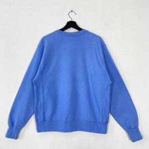 Peut inclure: Un sweat-shirt bleu clair &agrave; col rond, suspendu &agrave; un cintre noir sur fond blanc. Le sweat-shirt a des manches longues et des poignets et un ourlet c&ocirc;tel&eacute;s. Le tissu semble &ecirc;tre une mati&egrave;re douce et confortable.