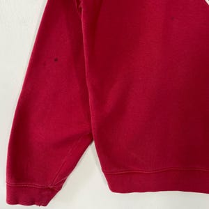 K&ouml;nnte beinhalten: Nahaufnahme eines roten Sweatshirts. Das Sweatshirt hat einen Rundhalsausschnitt und lange &Auml;rmel. Auf dem &Auml;rmel befinden sich ein paar kleine dunkle Flecken. Der Stoff scheint ein weiches Strickmaterial zu sein.