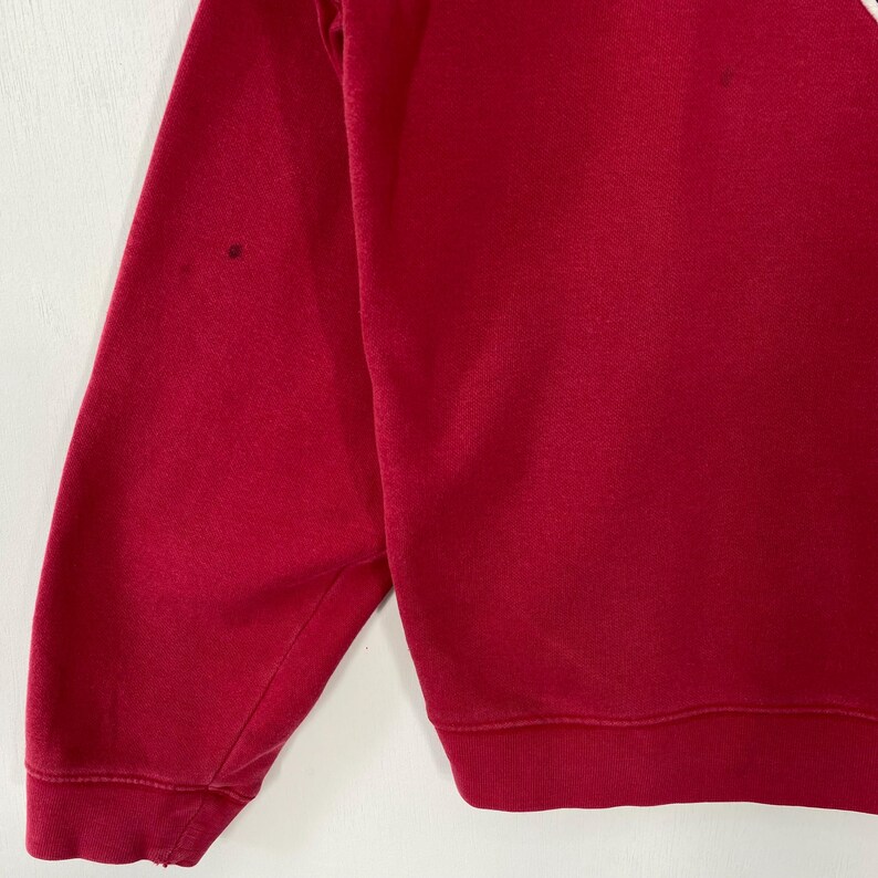 K&ouml;nnte beinhalten: Nahaufnahme eines roten Sweatshirts. Das Sweatshirt hat einen Rundhalsausschnitt und lange &Auml;rmel. Auf dem &Auml;rmel befinden sich ein paar kleine dunkle Flecken. Der Stoff scheint ein weiches Strickmaterial zu sein.