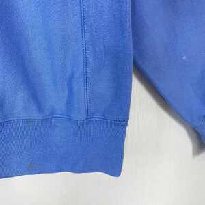 Peut inclure: Un sweat-shirt bleu clair avec un ourlet et des poignets c&ocirc;tel&eacute;s. Le v&ecirc;tement a un col rond et un d&eacute;tail de couture cousu sur le c&ocirc;t&eacute;. Le tissu semble &ecirc;tre une mati&egrave;re douce et confortable. Il y a quelques petites taches sur le tissu.