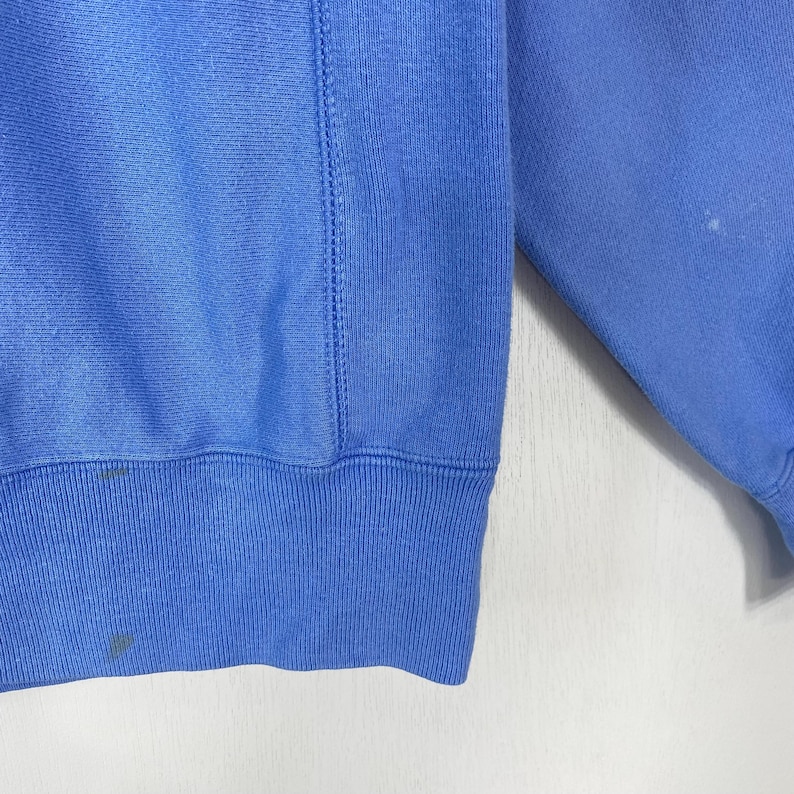 Peut inclure: Un sweat-shirt bleu clair avec un ourlet et des poignets c&ocirc;tel&eacute;s. Le v&ecirc;tement a un col rond et un d&eacute;tail de couture cousu sur le c&ocirc;t&eacute;. Le tissu semble &ecirc;tre une mati&egrave;re douce et confortable. Il y a quelques petites taches sur le tissu.