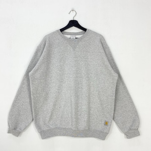 Peut inclure: Un sweat-shirt gris chiné est suspendu à un cintre noir sur fond blanc. Le sweat-shirt à col ras du cou a des manches longues et un ourlet et des poignets côtelés. Un petit logo carré jaune et marron est en bas à droite.
