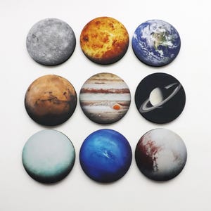 May include: Nine round magnets featuring images of the planets in our solar system. The planets are arranged in a 3x3 grid. The planets are: Mercury, Venus, Earth, Mars, Jupiter, Saturn, Uranus, Neptune, and Pluto.