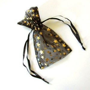 May include: A black sheer drawstring bag with gold stars printed on it. The bag is made of a delicate, translucent material and has a black ribbon drawstring.
