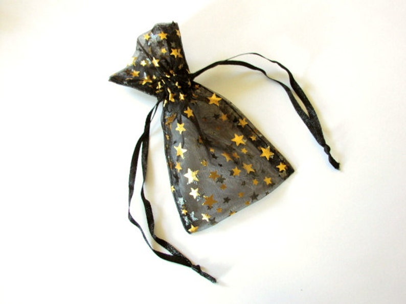 May include: A black sheer drawstring bag with gold stars printed on it. The bag is made of a delicate, translucent material and has a black ribbon drawstring.