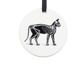 May include: A white ceramic ornament with a black silhouette of a cat skeleton. The ornament has a black ribbon for hanging.