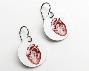 May include: A pair of silver earrings with a white background and a red anatomical heart illustration.