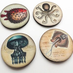 May include: Four round wooden coasters with vintage illustrations of sea creatures. The coasters feature a pufferfish, an octopus, a jellyfish, and a ray. The coasters are printed with a light brown background and black text.