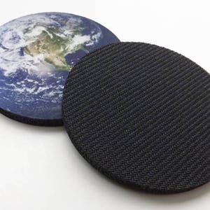 Pu&ograve; includere: Un sottobicchiere rotondo con un'immagine stampata della Terra su un lato e una superficie nera testurizzata antiscivolo sull'altro lato.
