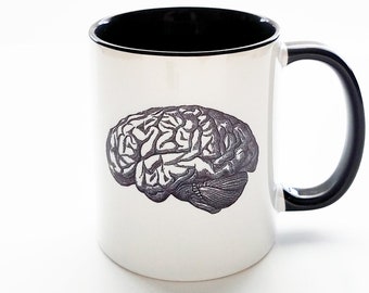 May include: White ceramic mug with a black rim and handle. The mug features a black and white illustration of a human brain.