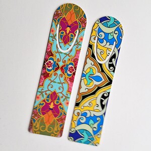 May include: Two decorative bookmarks with colorful, ornate patterns. One bookmark features a teal background with floral and geometric designs in pink, orange, and green. The other has a yellow background with blue, black, and gold patterns. Both have a metal clip.