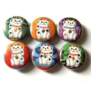 May include: Six round button pins featuring a white Maneki-Neko, or lucky cat, with black spots and a gold coin. Each pin has a different colorful background with floral and geometric patterns.