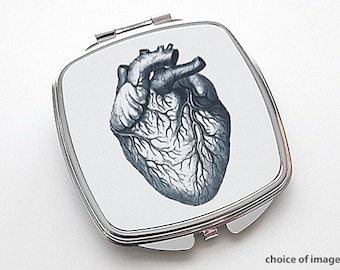 May include: A silver compact mirror with a white background and a black and white anatomical heart illustration.