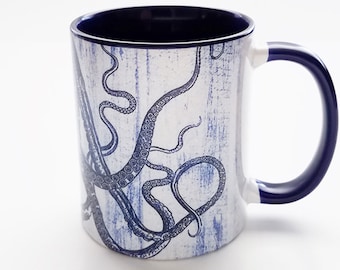 May include: A white ceramic mug with a blue rim and handle. The mug features a blue and white illustration of an octopus with its tentacles wrapping around the mug.