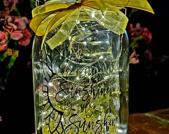 May include: A mason jar with a yellow ribbon and string lights inside. The jar has a black vinyl decal that says "You are my sunshine, my only sunshine".