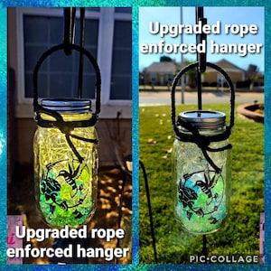 May include: A glass jar with a solar light inside, decorated with green and blue glass beads and a hummingbird silhouette. The jar is hanging from a black rope and a metal hook. The text "Upgraded rope enforced hanger" is visible in the image.