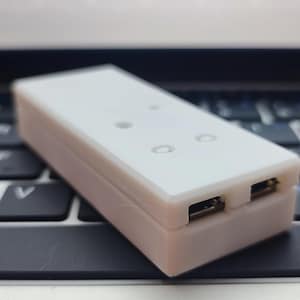 Op de afbeelding: Een witte USB-hub met drie poorten en twee LED's op een laptoptoetsenbord.
