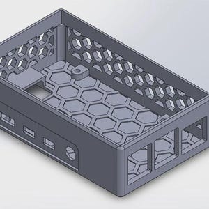 Op de afbeelding: Een grijs rechthoekig omhulsel met een honingraatpatroon op de bodem en zijkanten. De behuizing heeft rechthoekige uitsparingen en een klein rond gat. De bovenkant heeft een zeshoekig patroon.